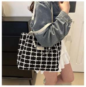 Detail of checkered tote bag with pearl chain decoration on female model shoulder