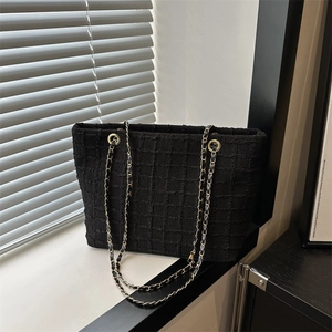 Large black textured tote bag with gold chain shoulder strap in minimalist style