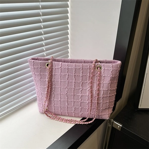 Pink woven tote bag with gold chain strap placed on a window sill in soft light