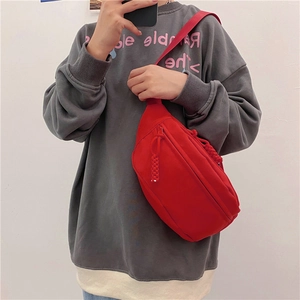 Detalle de bolso bandolera de lona roja con textura y tirador de cremallera trenzado