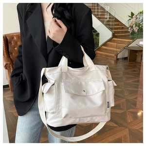 Detail of a beige canvas tote bag with functional side pockets and adjustable strap