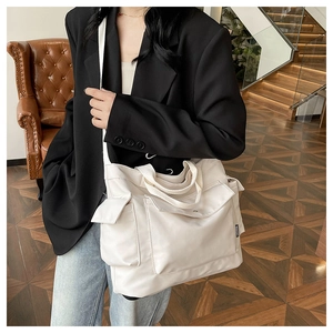 Detail of white multi-pocket tote bag showing the side fashion label and wide strap
