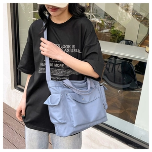 Close-up of light blue multi-pocket nylon crossbody bag with fashion label and wide strap