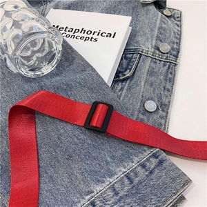 Detalle de correa de lona roja tejida con hebilla negra ajustable sobre denim