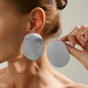Nahaufnahme eines Models mit großen unregelmäßigen silbernen Metall-Ohrsteckern in glänzendem Finish