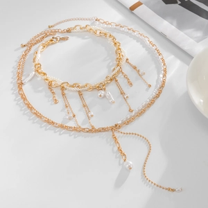 Collana a strati dorata con perle irregolari e nappe su una superficie bianca