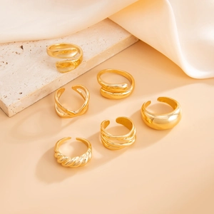 Detail of six-piece gold liquid metal rings set on beige textured stone and white silk