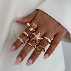 Detail shot of a gold starfish and shell ring set with pearl accents on a hand