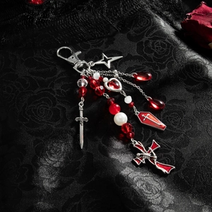 Close-up of gothic cross, sword, and red coffin charms on a black rose satin backdrop