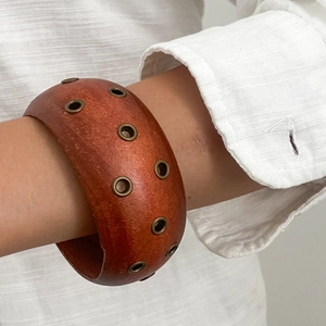 Dettaglio di un ampio bracciale in legno rosso-marrone con occhielli in metallo vintage