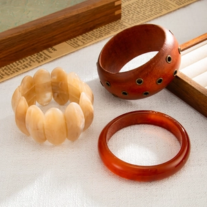 Tre eleganti bracciali rigidi in legno e resina disposti su una superficie materica