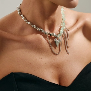Dettaglio della collana con cuore d'argento, pietre verdi e frange indossata dal modello