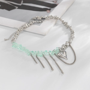 Dettaglio della collana di perline argentate con pietre verdi, cuore e nappe in metallo