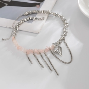 Collana con pendente a cuore, pietre rosa e nappe metalliche su un tavolo minimalista