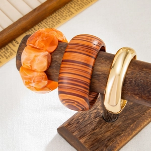 Dettaglio di bracciali in resina, legno e metallo dorato su un supporto per gioielli
