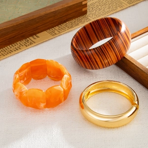 Dettaglio di bracciale in legno, braccialetto in resina arancione e polsino in metallo oro