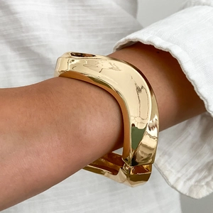 Dettaglio ravvicinato di un ampio bracciale dorato irregolare con finitura lucida a specchio