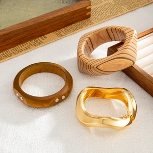 Dettaglio di bracciali in legno e metallo dorato ondulato su un vassoio neutro