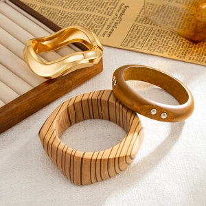 Dettaglio di un bracciale dorato ondulato, un cerchio giallo e un ampio bracciale in legno