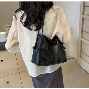 Detail view of large black leather tote bag with side drawstring knots on female model
