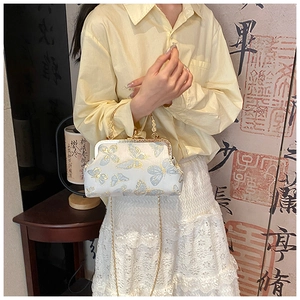 Dettaglio del ricamo a farfalla blu su borsa da sera in seta beige con manico in metallo