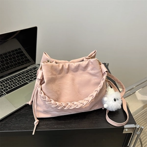Borsa hobo rosa con manico intrecciato e ciondolo di peluche su scrivania nera