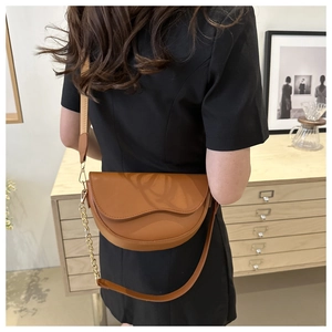 Brown matte leather saddle bag with gold chain strap shown on a woman in a minimal setting