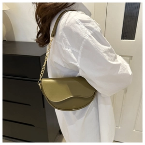 Olive green half-moon crossbody bag with elegant gold chain strap worn by a model