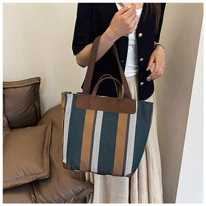 Dettaglio di una borsa tote capiente con strisce verticali verdi e gialle e manici in pelle