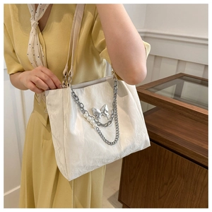 Détail d'un sac cabas blanc avec breloque papillon argentée et chaîne de perles chic