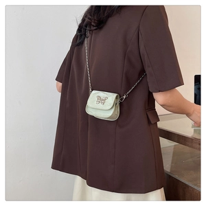 Dettaglio mini borsa a tracolla verde menta con fibbia a farfalla su blazer marrone