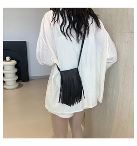Detailed view of a black crossbody bag with long fringes and slim strap on white shirt