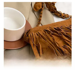 Dettaglio borsa scamosciata marrone con frange, tracolla intrecciata e stile boho