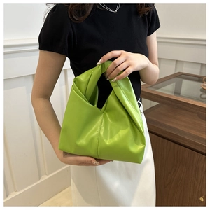 Dettaglio della borsa a mano verde brillante pieghettata con nodo tenuta da una modella