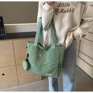 Dettaglio della borsa tote in tela verde con ricami di lettere colorate e bustina tonda