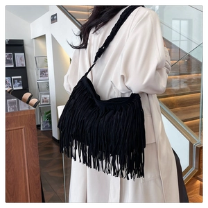 Dettaglio della borsa hobo boho nera con lunghe frange e tracolla intrecciata su modella