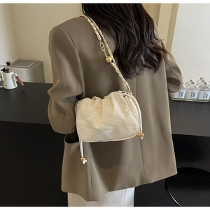 Dettaglio borsa a nuvola beige plissettata con catena dorata in un ambiente di caffè