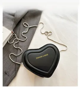 Close-up of heart-shaped black crossbody bag featuring gold letters and silver chain