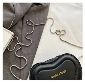 Close-up of heart-shaped black leather bag with silver snake chain on a textured surface