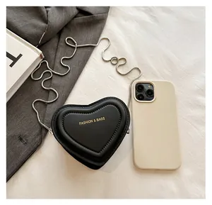 Detail of a black heart-shaped crossbody bag with a silver chain next to a smartphone