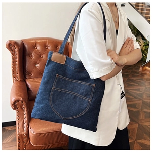 Dettaglio borsa tote in denim blu scuro con cuciture gialle e toppa in pelle marrone