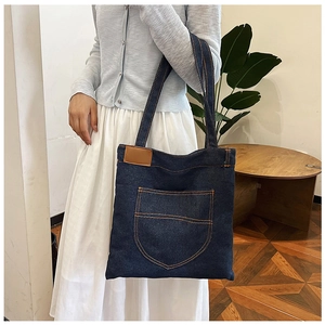 Dettaglio della borsa tote in denim blu con cuciture e applicazione in cuoio