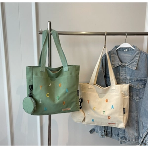 Dettaglio di borse tote in tela con ricamo a lettere colorate e mini pochette tonde abbinate