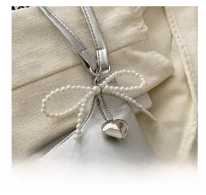 Détail d'un sac seau argenté avec nœud en perles et pendentif en métal en forme de cœur