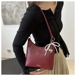 Détail du sac seau bordeaux avec nœud en perles et pendentif cœur argenté élégant