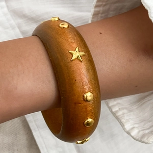 Dettaglio di un ampio bracciale in legno boho con borchie a stella e rivetti dorati