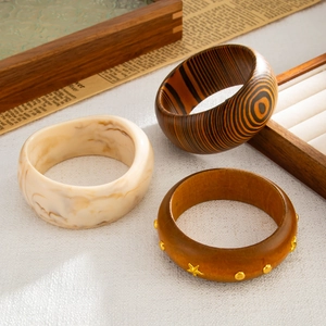 Dettaglio di bracciali geometrici in resina e legno con rivetti dorati e trama marmorizzata