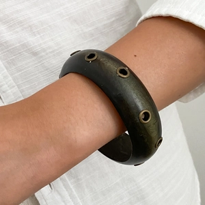 Dettaglio di un bracciale largo in resina con rivetti metallici indossato al polso