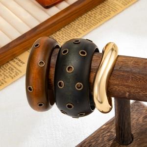 Dettaglio di bracciali a trama legno con occhielli in metallo e polsino dorato lucido
