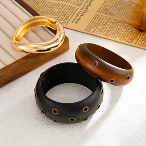 Dettaglio di bracciali geometrici dorati e in legno largo con occhielli metallici